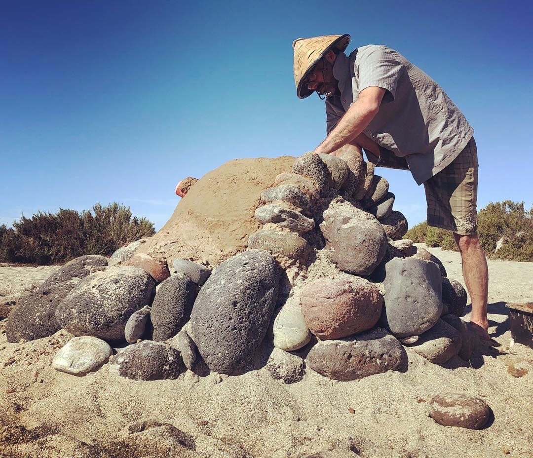 Stacking rocks and sand into a domed clay oven on a beach in Baja.