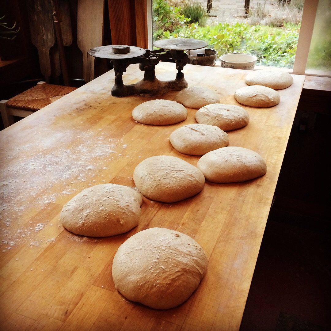 Rounds of shaped dough resting on a floured wooden table beside a balance scale.