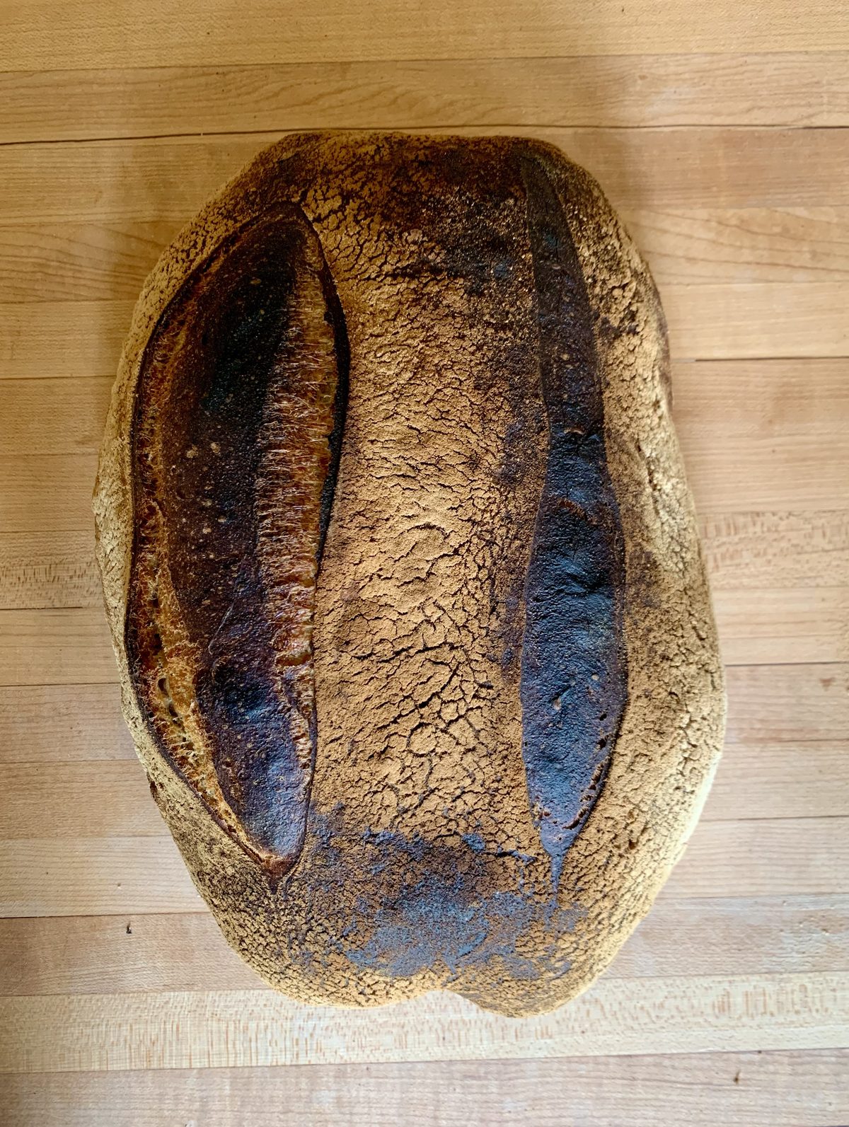 A whole loaf of pain de campagne on a wooden board, its dark crust split along two long scores.