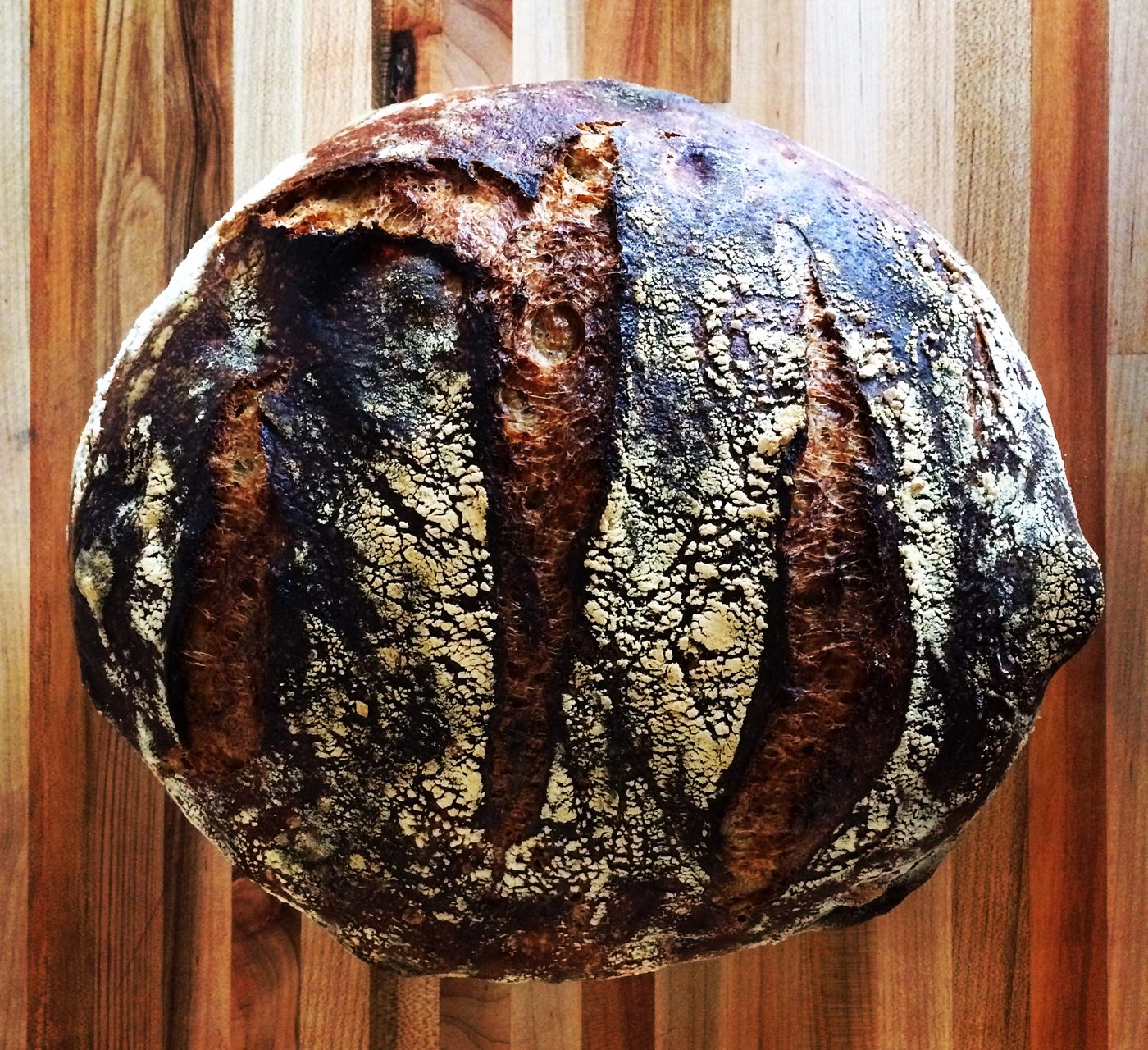 A dark, deeply scored round sourdough loaf resting on a wooden board.