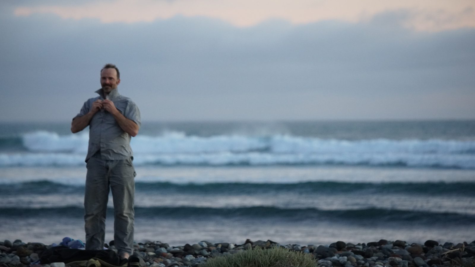 A person standing at the shoreline looking out at a grey, rolling sea.